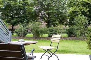Un espace extérieur aménagé avec une table et deux chaises, entouré de verdure et d’arbres.