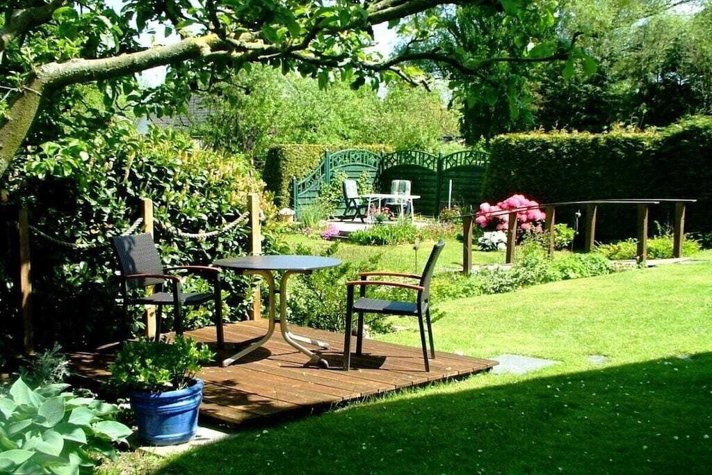 Un patio exterior con una mesa y sillas, rodeado de follaje y un seto.
