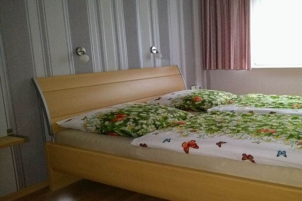Un letto singolo con una testiera in legno, una coperta a motivi floreali e cuscini coordinati.