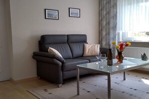 A modern living room with a dark grey sofa, a glass coffee table, and a vase with flowers. - Holiday apartment with 1 bedroom (Kühlungsborn Ost)