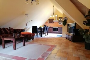 A loft-style living area with a dining table, sofa, and kitchen in the background. - Holiday apartment Sterntaucher 04 (Ostseebad Ahrenshoop)