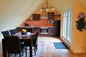 A dining area with a table and chairs, a kitchen with appliances, and a window with a view. - Holiday apartment Sterntaucher 04 (Ostseebad Ahrenshoop)