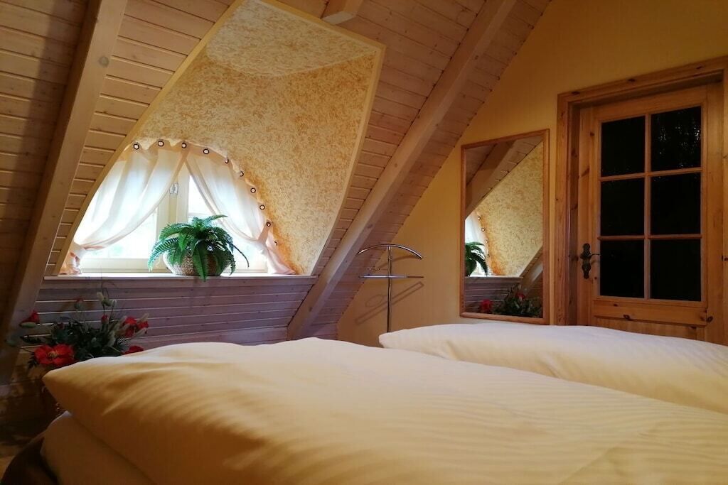 A bedroom with a sloped ceiling, a window with curtains, a bed, and a door.