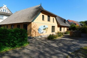 A traditional building with a thatched roof, a mural on the side, and a paved driveway. - Holiday apartment Sterntaucher 04 (Ostseebad Ahrenshoop)
