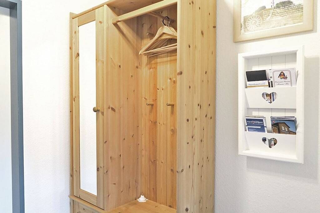 Een houten garderobe met spiegel, een kledingroede en een witte muur met een lijstfoto en een klein plankje met spullen.