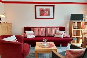 A living room with a red sofa, two armchairs, a coffee table, a TV, and a bookshelf. - Holiday apartment in Waren with swimming pool (Waren)