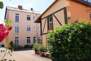 A courtyard with a building featuring a traditional half-timbered facade, a brick pathway, and potted plants. - Holiday apartment in Waren with swimming pool (Waren)