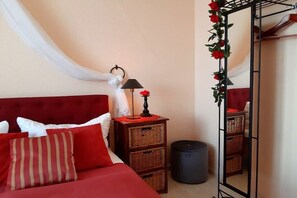 A bedroom with a red bed, white pillows, a bedside lamp, wicker baskets, a trash can, and a mirror with red roses. - Holiday apartment in Waren with swimming pool (Waren)