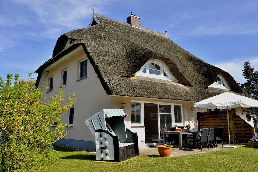 Una casa con un tetto di paglia, un patio con mobili da esterno e un giardino.