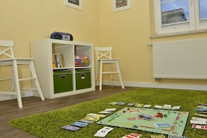 A room with a green carpet, a bookshelf, two white chairs, and a Monopoly board game. - Holiday home in Born on the Darß peninsula with Wi-Fi (Born auf dem Darß)