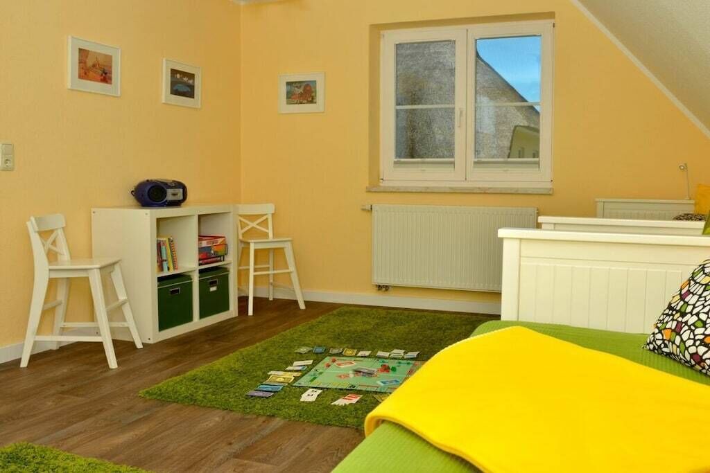 Ein Kinderzimmer mit Bücherregal, zwei Stühlen, einer Heizung und einem Fenster.