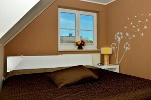 A bedroom with a bed, a window, a bedside table with a lamp, and a wall decoration. - Holiday home in Born on the Darß peninsula with Wi-Fi (Born auf dem Darß)