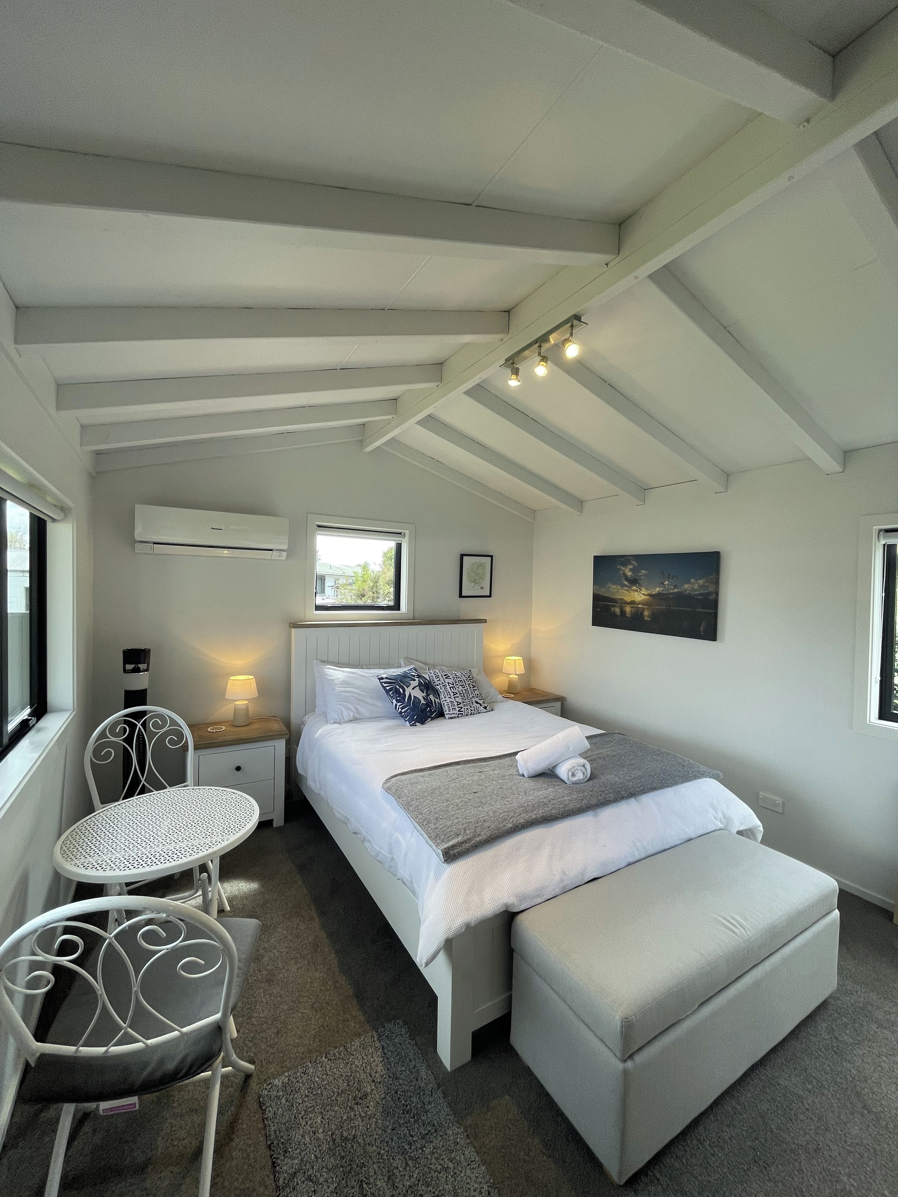 Een slaapkamer met een bed, nachtkastjes, een stoel, een raam en een airconditioning.