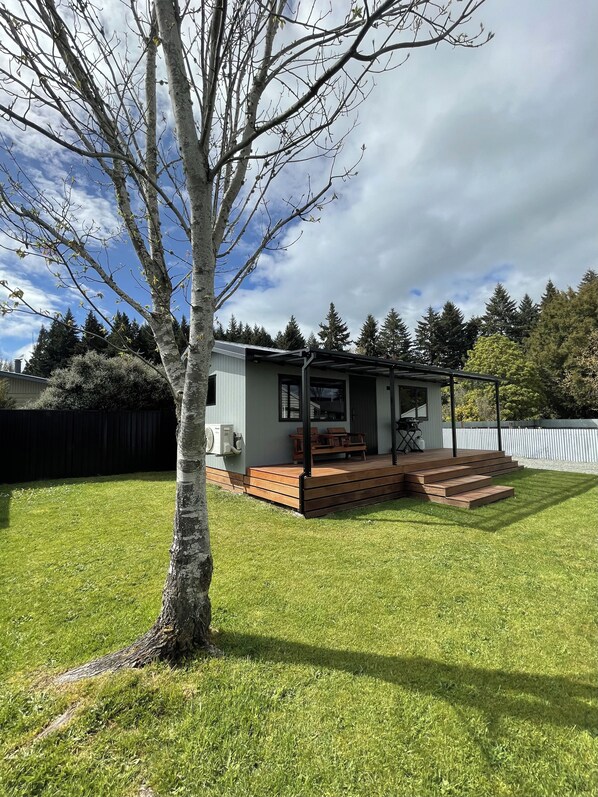 A small, single-story building with a porch and steps, surrounded by a well-maintained lawn and trees.