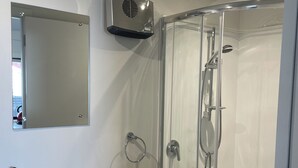 A modern bathroom with a glass-enclosed shower, a white sink with a wooden shelf, and a mirror above the sink. - Romantic 1-bedroom guesthouse with all the extras! (Te Anau)