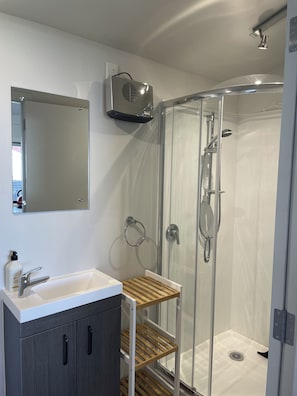 Un baño moderno con ducha acristalada, un lavabo blanco con estante de madera y un espejo sobre el lavabo.