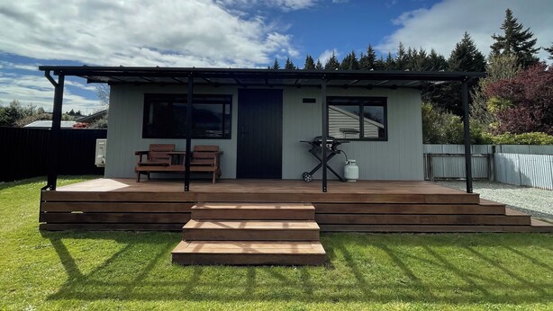 A modern house with a covered porch, a wooden deck, and a well-maintained lawn. - Romantic 1-bedroom guesthouse with all the extras! (Te Anau)