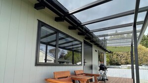 A covered outdoor area with a wooden bench and a grill. - Romantic 1-bedroom guesthouse with all the extras! (Te Anau)