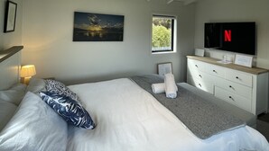 A bedroom with a bed, a dresser, a painting, a window, and a TV. - Romantic 1-bedroom guesthouse with all the extras! (Te Anau)
