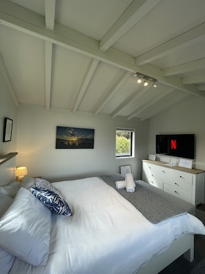 Un dormitorio con cama, cómoda, cuadro, ventana y televisor.