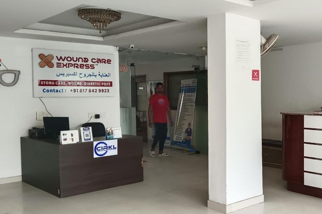 A reception area with a sign for Wound Care Express, a reception desk, and a person in a red shirt walking in the background.