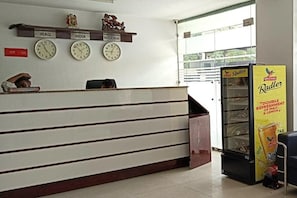 A reception area with clocks displaying times from Iraq, India, and Nigeria, a Radler refrigerator, and a sign indicating a 12-hour service window. - Hotel Starr Residancy (gurugram)