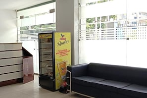 A Radler vending machine and a blue sofa in a room with a glass partition and a view of buildings outside. - Hotel Starr Residancy (gurugram)