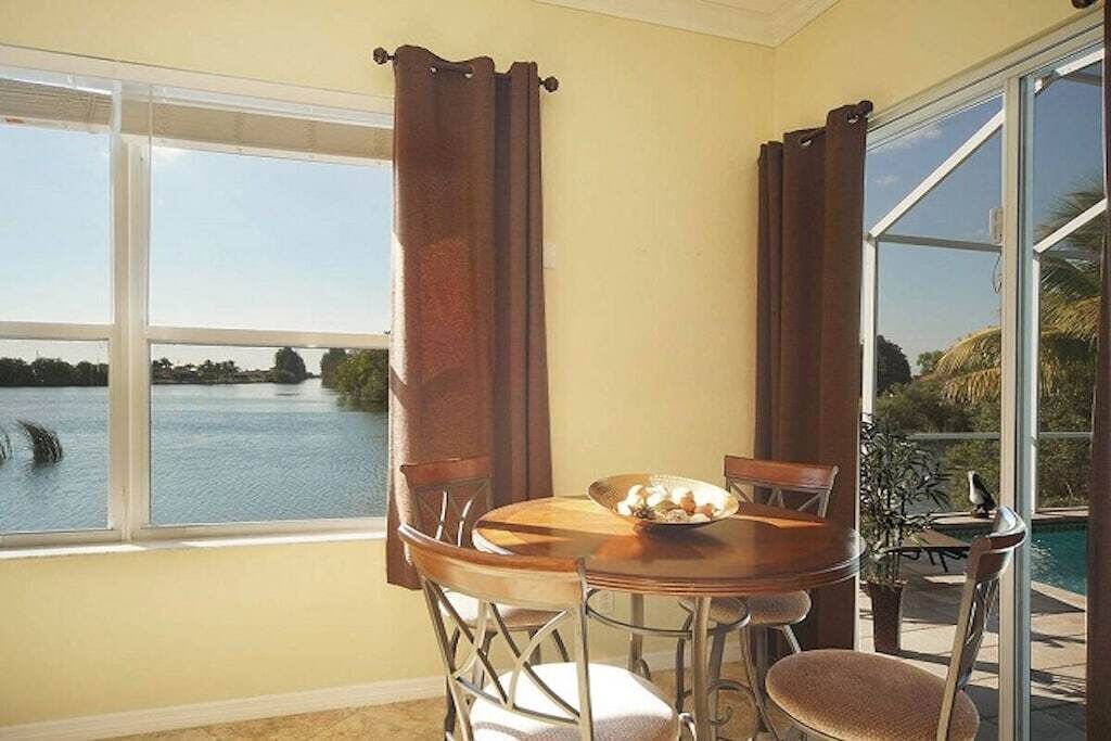 Un comedor con vista a un lago, una mesa con sillas y una ventana con cortinas.
