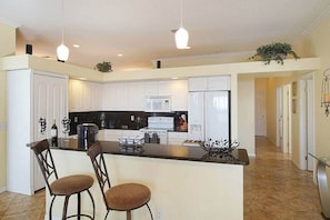 A modern kitchen with white cabinets, a central island with bar stools, and pendant lighting. - Villa in Cape Coral with swimming pool (Cape Coral)
