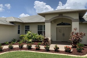 A two-story house with a front entrance, a covered porch, and a landscaped garden with various plants and flowers. - Villa in Cape Coral with swimming pool (Cape Coral)