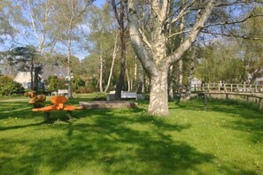 A park with a large tree, a wooden bridge, and a playground with orange equipment. - Holiday apartment with 2 bedrooms (Dierhagen)