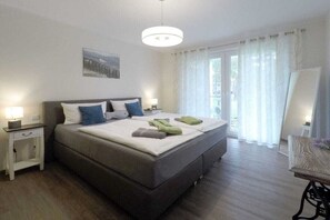 Ein Schlafzimmer mit einem Bett, Nachttischen, einer Pendelleuchte und einem Fenster mit Vorhängen.