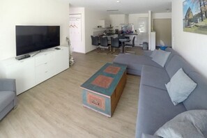 A modern living room with a flat-screen TV, a grey sofa, a coffee table, and a kitchen area in the background. - Holiday apartment with 2 bedrooms (Dierhagen)