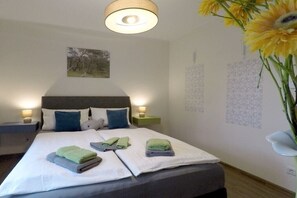 A neatly made bed with pillows and folded towels, a wall-mounted artwork, and a vase with sunflowers. - Holiday apartment with 2 bedrooms (Dierhagen)