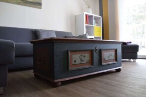 Eine dunkle Holzkiste mit zwei gerahmten Bildern, ein graues Sofa und ein weißes Regal mit bunten Aufbewahrungsboxen.