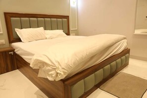 A bed with a wooden frame and upholstered headboard, a white mattress, and a matching pillow. - Aachman Hotal Restaurant (Bulandshahr)