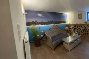 A room with a beach-themed mural, wicker furniture, a small table, and a stone wall. - Beach Villa Miramare / Apt. Sea Urchin (Klütz)