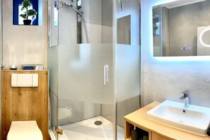 Ein modernes Badezimmer mit einer gläsernen Dusche, einem Holzwaschtisch mit Waschbecken und einer kleinen Toilette.