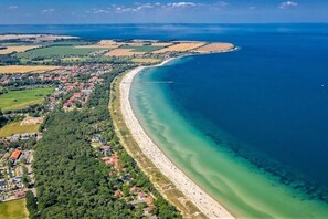 Luftaufnahme einer Küstenlandschaft mit Strand, einer kleinen Insel und einer Stadt mit Häusern und Grünflächen.