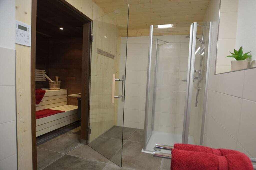 A glass-enclosed shower area with a wooden bench and a red towel.