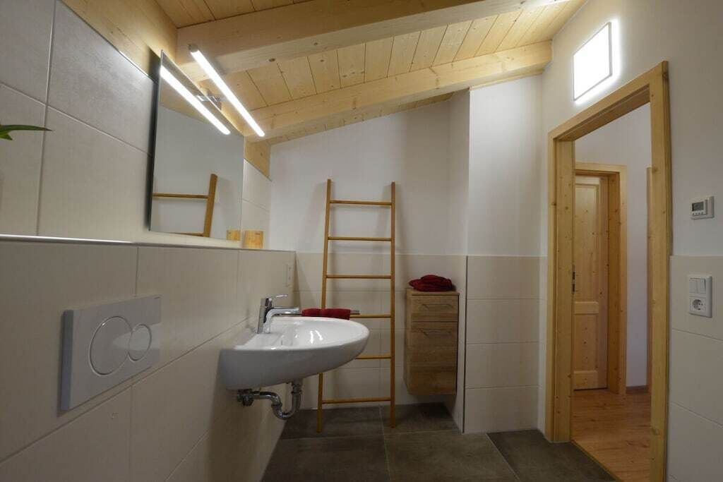 A bathroom with a white sink, a wooden ladder, and a wooden door.