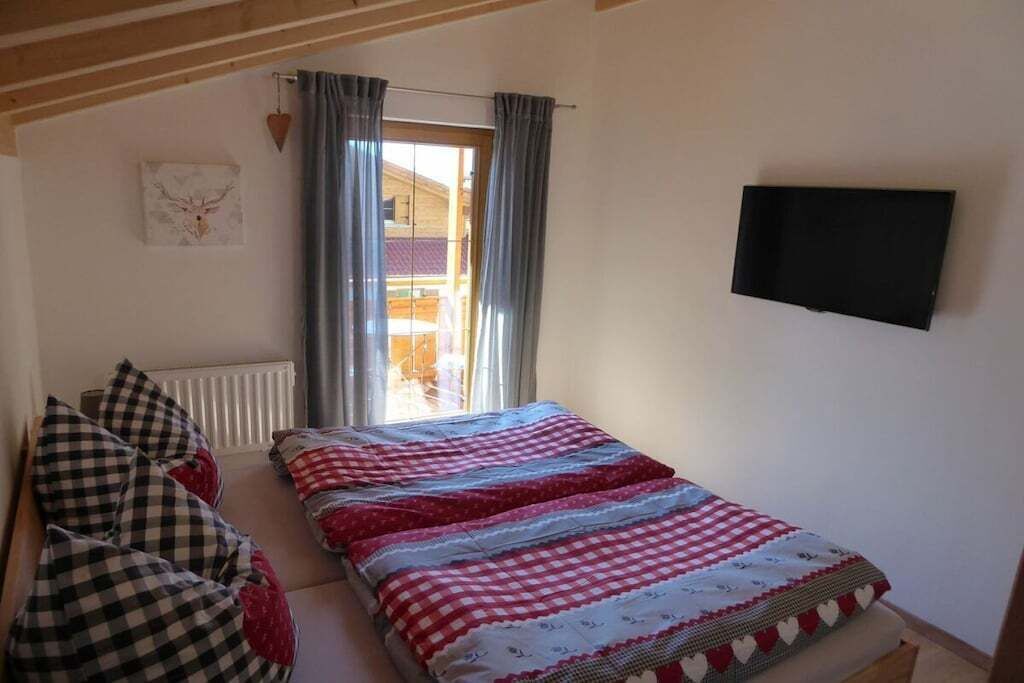 Een slaapkamer met een bed, een raam met gordijnen, een radiator, een flatscreen televisie en een aan de muur hangend schilderij.