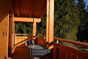 Un terrazzo in legno con tavolo e sedie, circondato da una ringhiera in legno, e vista sugli alberi sullo sfondo.