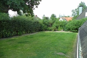 A grassy yard with a hedge, a stone wall, and a building with a red roof in the background. - North Sea holiday home Hoffmeister (Wurster Nordseeküste)