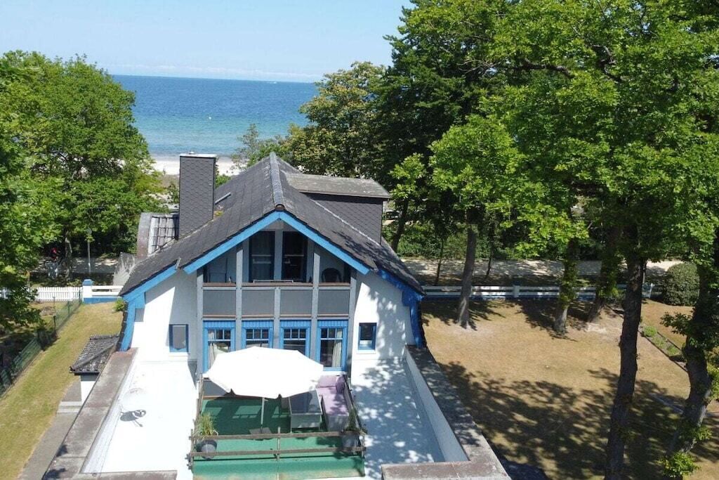 A two-story house with a blue and white exterior, a front porch with a green lawn, and a view of the ocean.