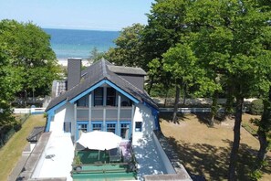 A two-story house with a blue and white exterior, a front porch with a green lawn, and a view of the ocean. - Beach villa Miramare, apartment Seestern (Ostsee Bad Boltenhagen)