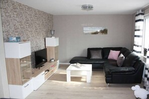 Ein Wohnzimmer mit Fernseher, einem weißen Couchtisch, einem schwarzen Ledersofa und einer Wand mit Steinmuster.