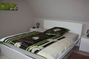 Ein Bett mit floralem Überwurf, ein Nachttisch mit Lampe und eine Wand mit einem Blumenbild.