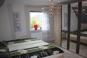 Ein Schlafzimmer mit einem großen Bett, einem Fenster mit Vorhängen, einem Heizkörper und einem Spiegel.