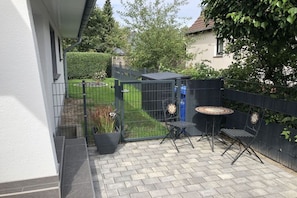 Eine Terrasse mit Tisch und Stühlen, ein kleiner Garten und ein Metallzaun.